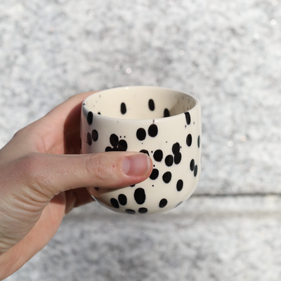 Latte coffee mug Black Dots made of stoneware with black and white glaze held in the hand.