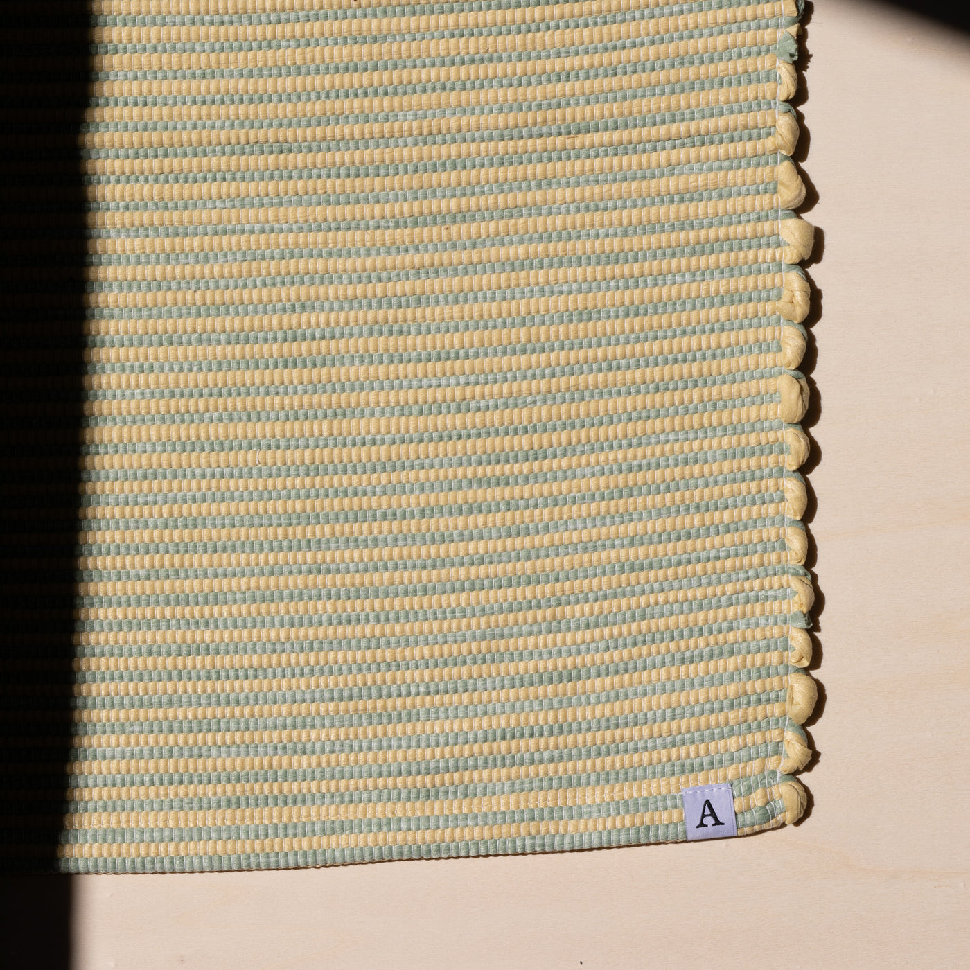 Close-up in sunlight of a striped bathroom rug in yellow and mint green
