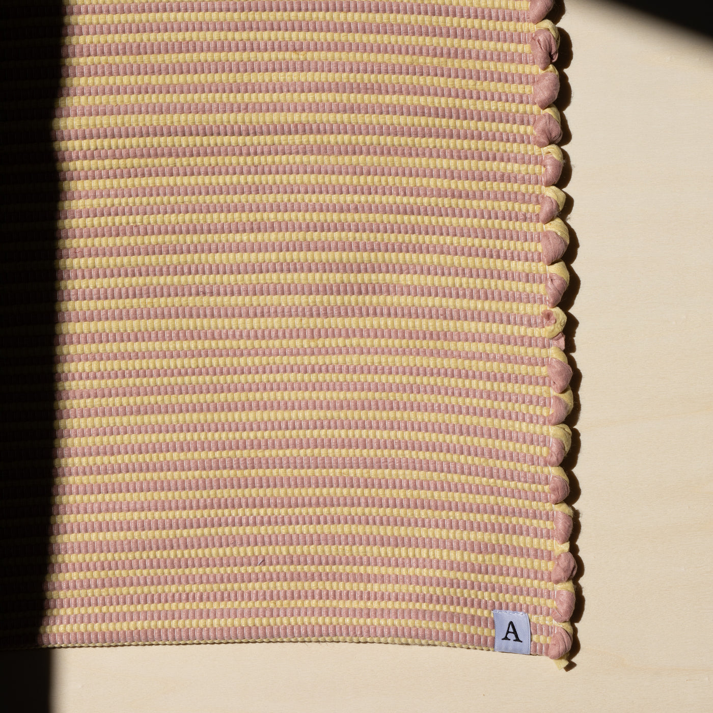 Close-up in the sunlight striped bathroom rug in yellow and pink handwoven from cotton remnants