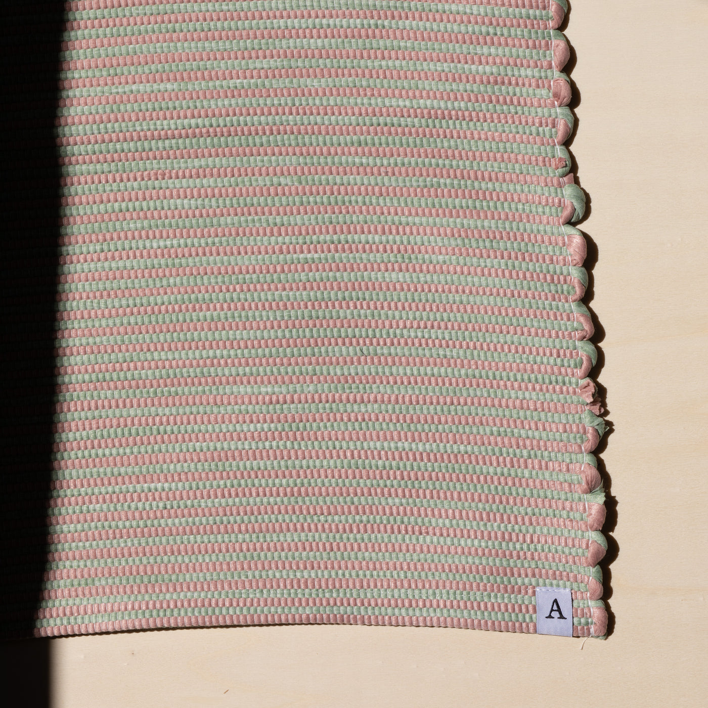Close-up in the sunlight of a striped bathroom rug in pink and mint green