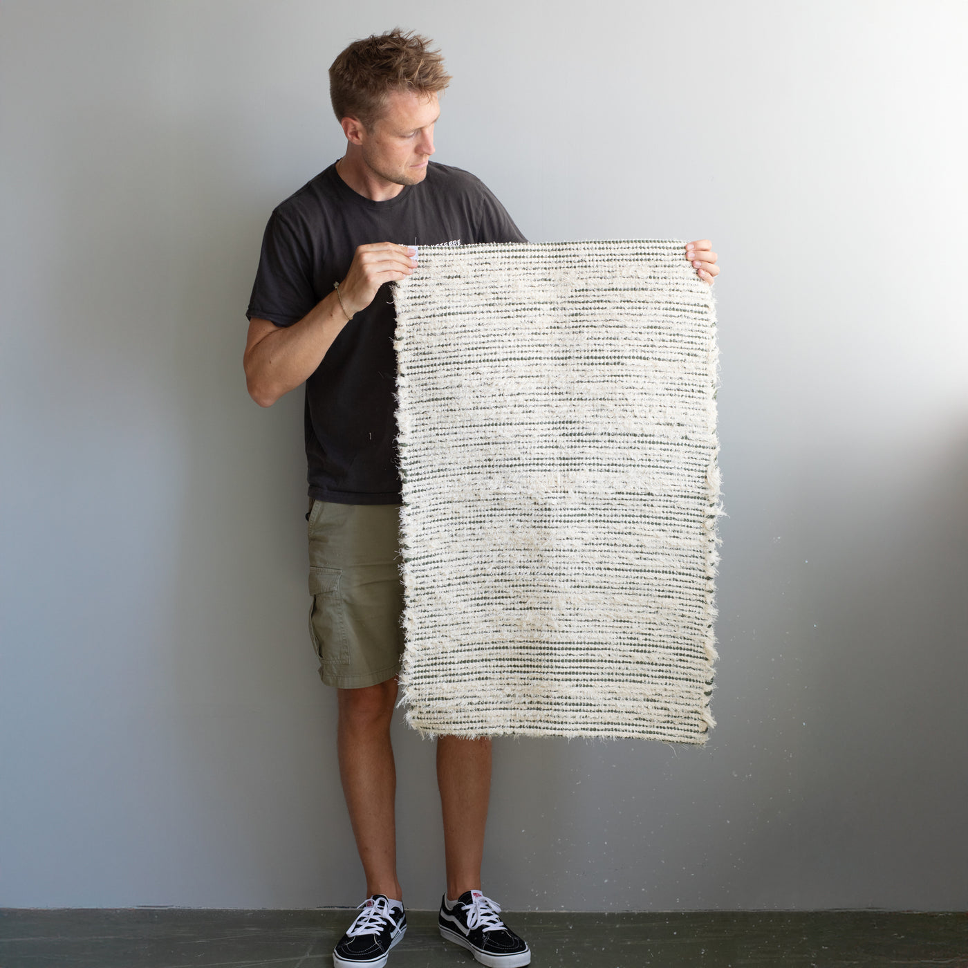 Terry bathroom rug held upright by a person with olive green stripes made from recycled fabric produced in Portugal