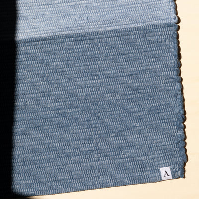 Close-up of the lower end of a small dark blue rug with the logo A by Atelier Agave