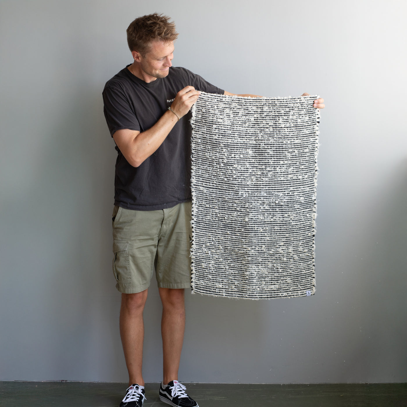 Small 60x90cm rug held by one person made of white terry cloth with black stripes hand-woven in Portugal