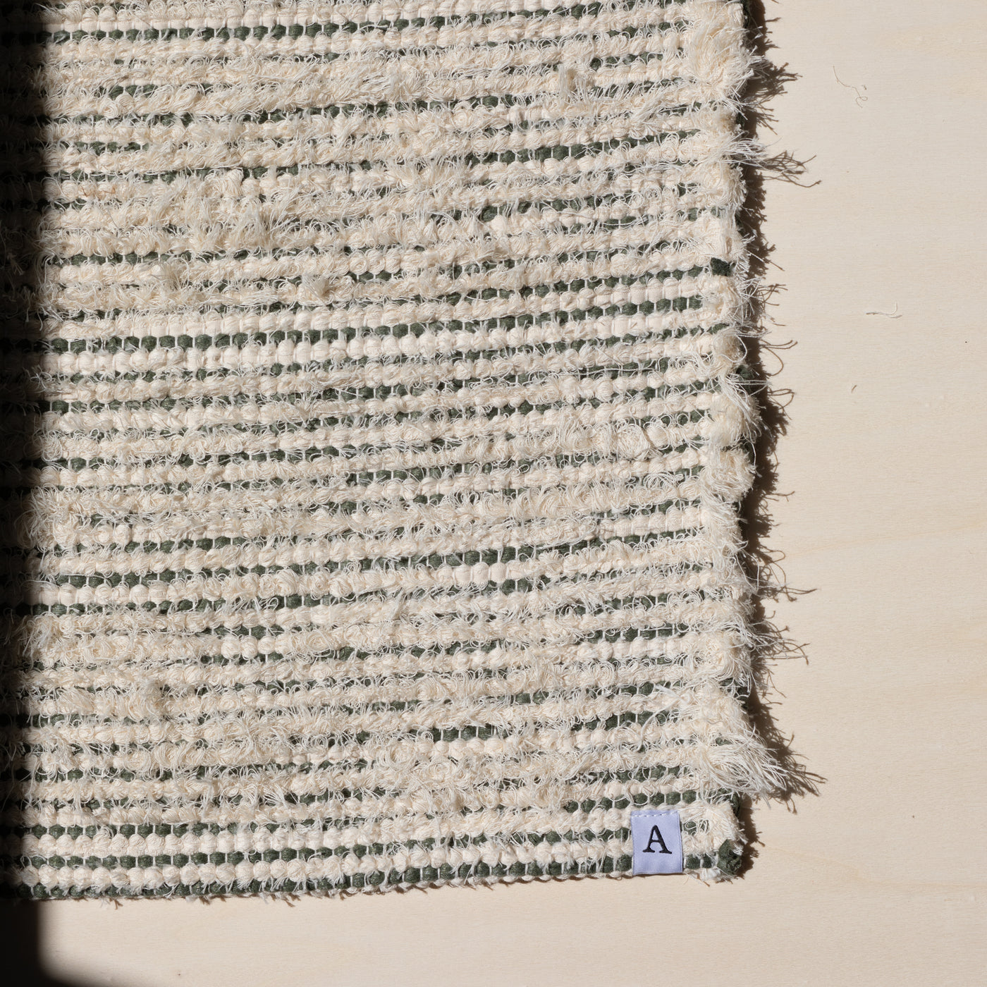 Closeup of a small rug 60x80cm striped with olive green cotton fabric and white terry cloth in the sunlight