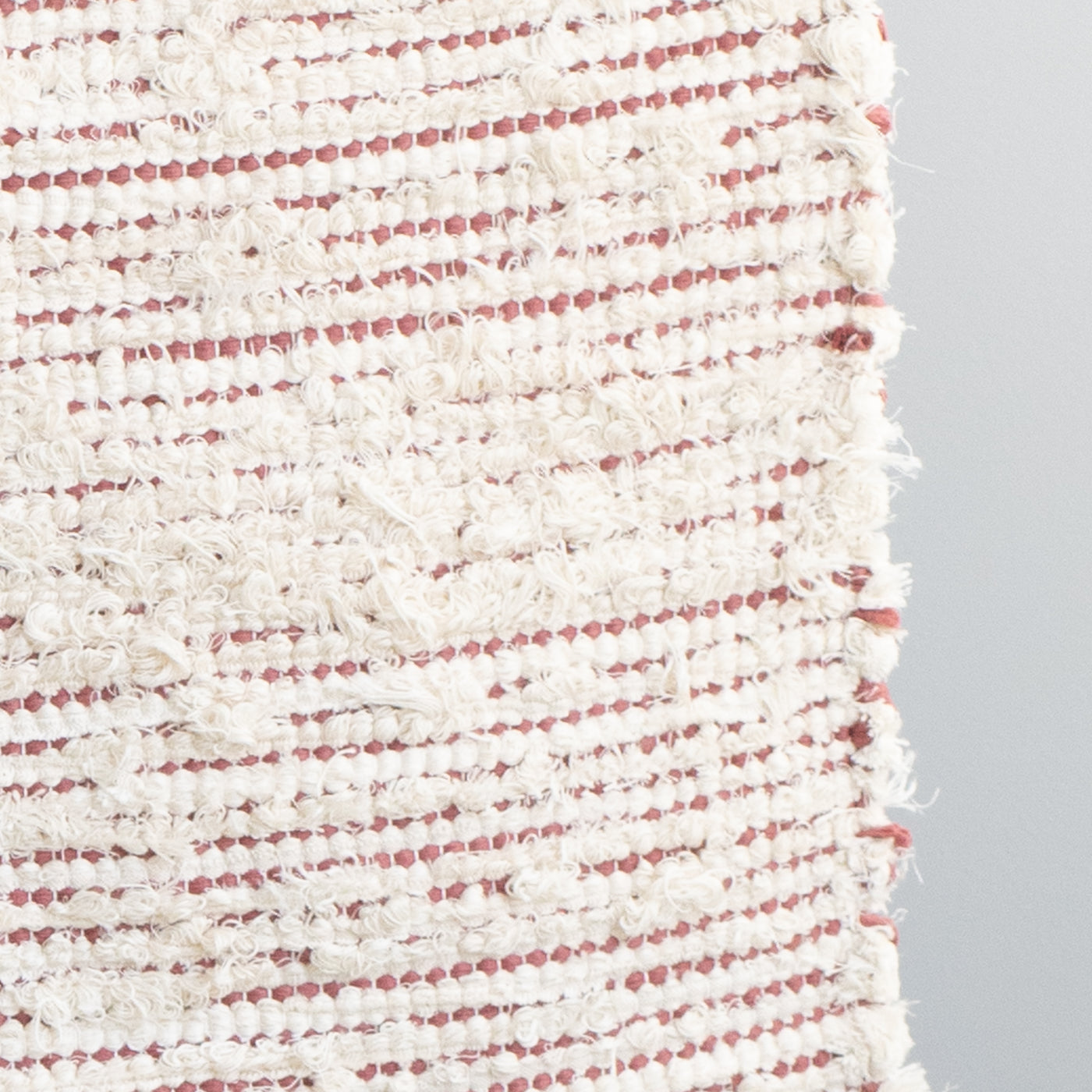 Closeup of a bathroom rug striped with peach-colored cotton fabric and white terrycloth hand-woven in Portugal