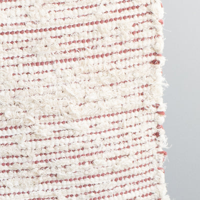 Closeup of a bathroom rug striped with peach-colored cotton fabric and white terrycloth hand-woven in Portugal