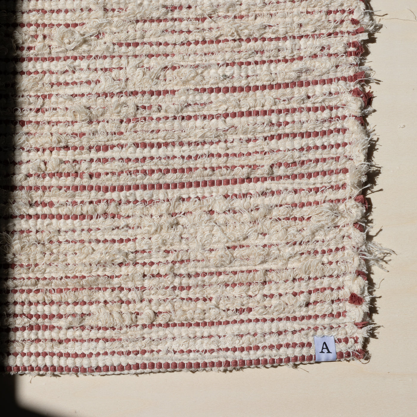 Closeup of a small rug 60x80cm striped with peach-colored cotton fabric and white terrycloth in the sunlight