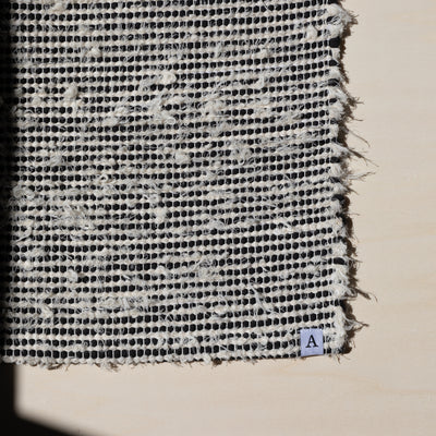 Closeup of a small carpet 60x80cm striped with black cotton fabric and white terry cloth in the sunlight