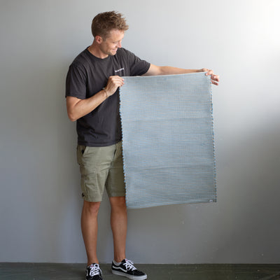 60x90cm small rug held by a person in light blue striped with jute hand-woven in Portugal