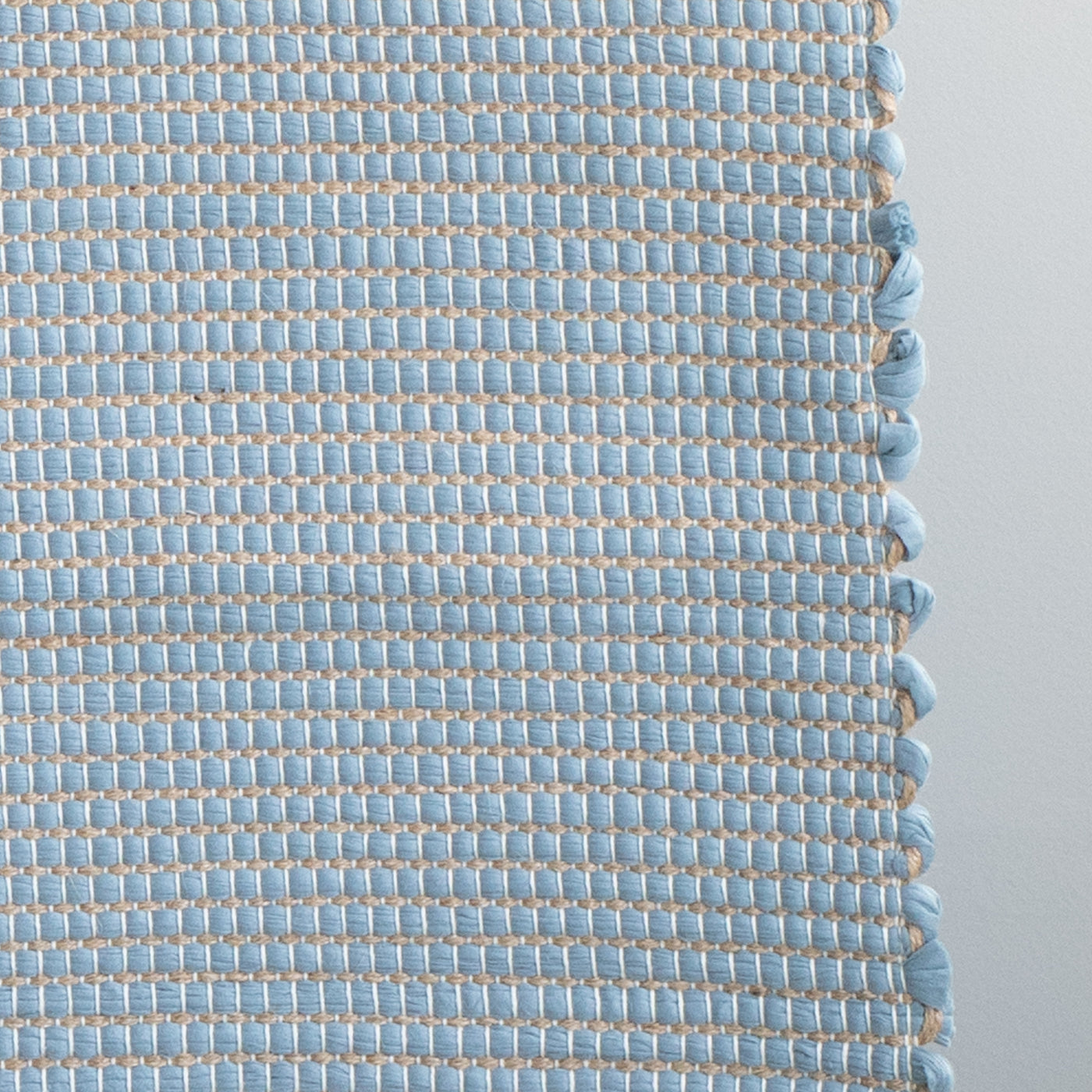 Closeup of a bathroom rug in light blue with jute stripes made from wool remnants from the textile industry, hand-woven in Portugal