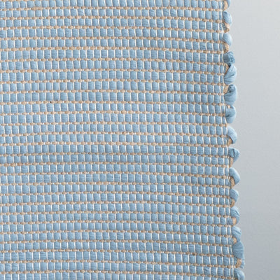 Closeup of a bathroom rug in light blue with jute stripes made from wool remnants from the textile industry, hand-woven in Portugal