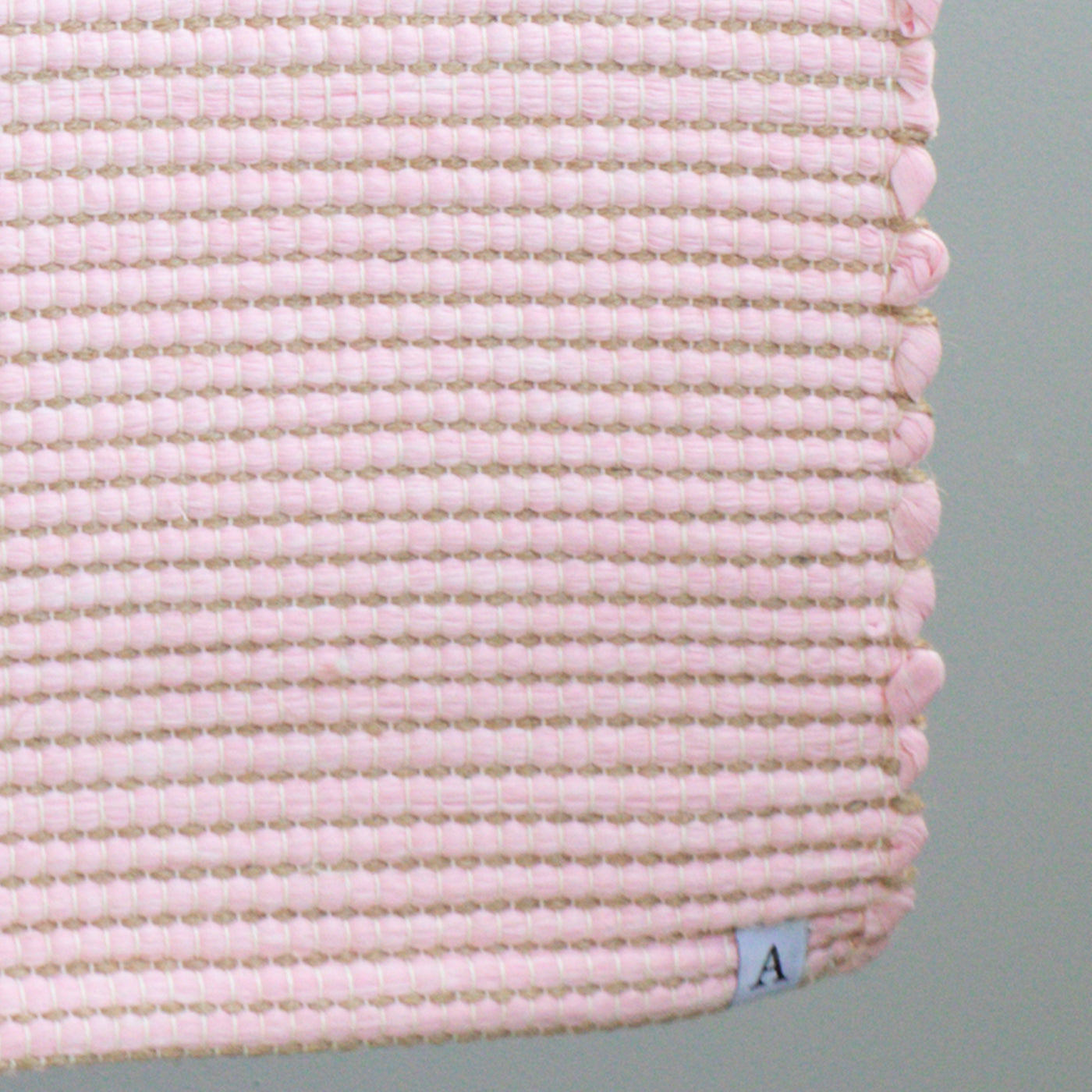 Close-up of a bathroom rug in pink with jute stripes made from wool remnants from the textile industry, hand-woven in Portugal