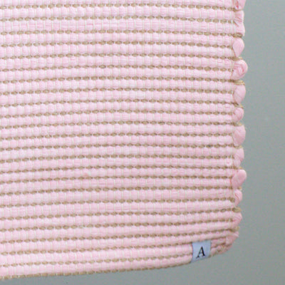 Close-up of a bathroom rug in pink with jute stripes made from wool remnants from the textile industry, hand-woven in Portugal