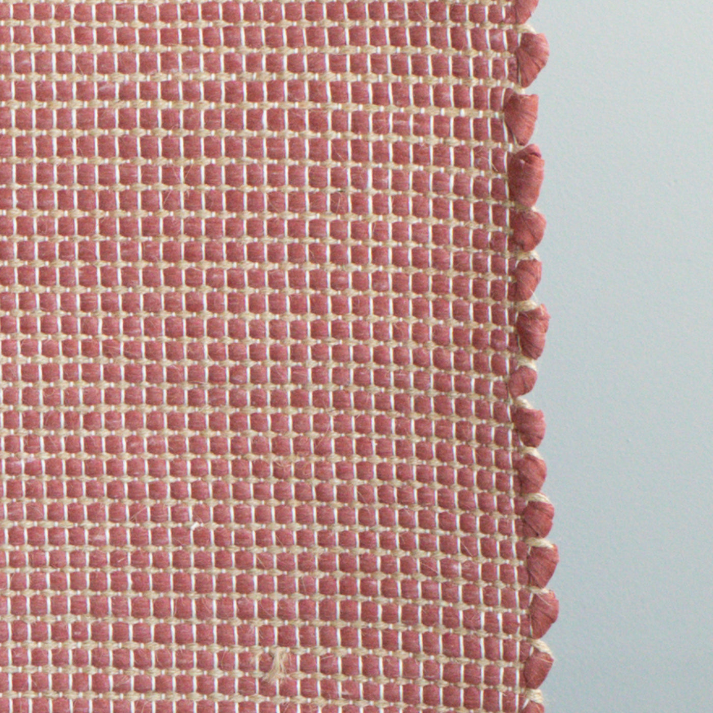 Close-up of a bathroom rug in red with jute stripes made from wool remnants from the textile industry, hand-woven in Portugal