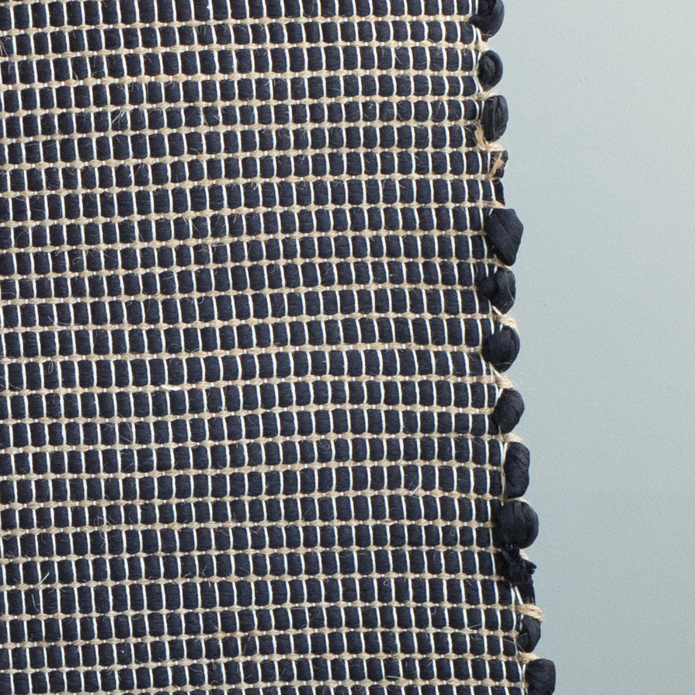 Close-up of a bathroom rug in black with jute stripes made from wool remnants from the textile industry, hand-woven in Portugal
