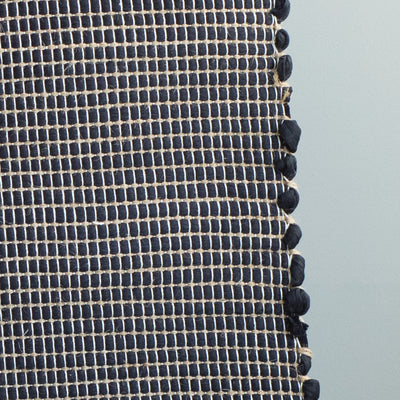 Close-up of a bathroom rug in black with jute stripes made from wool remnants from the textile industry, hand-woven in Portugal