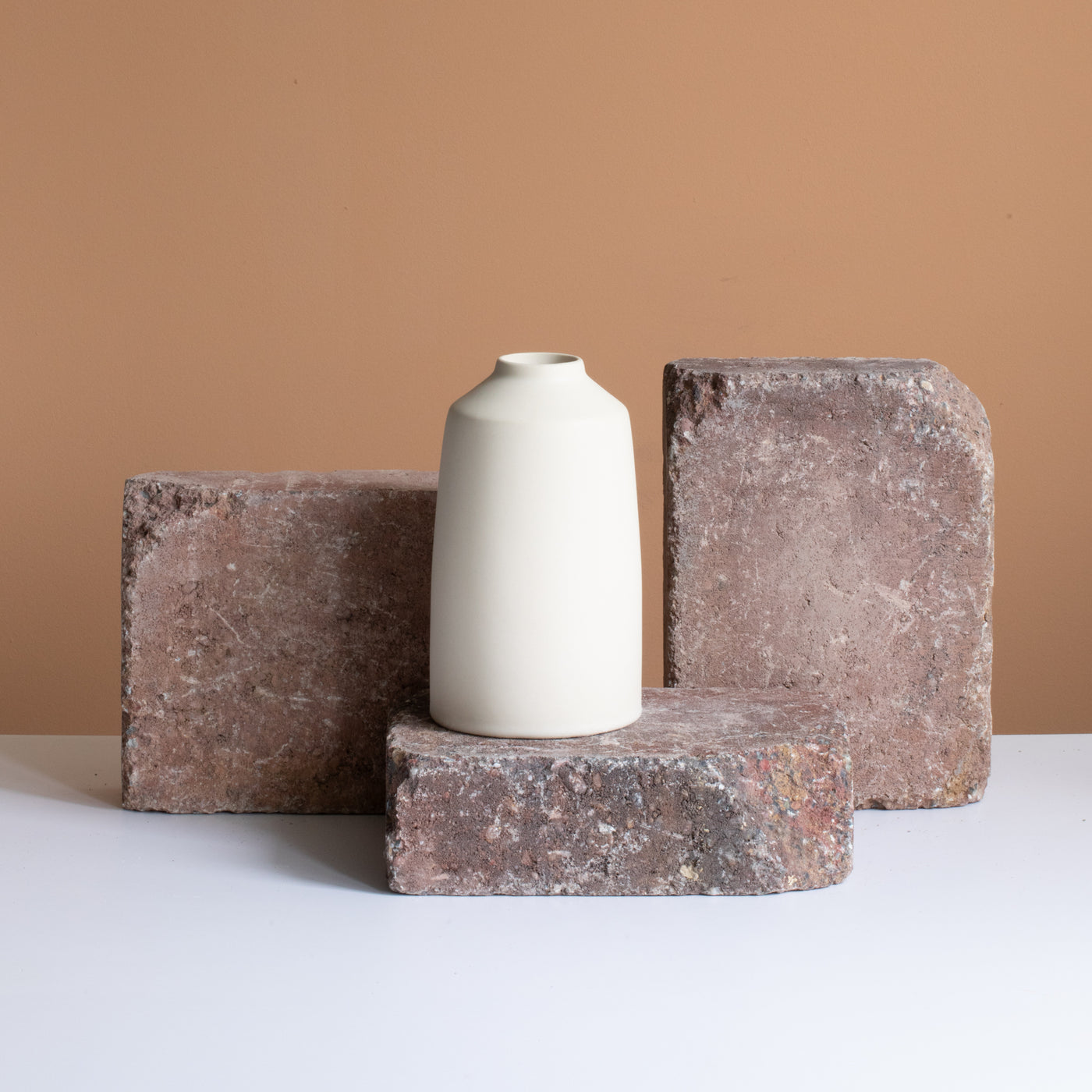 Beige flower vase stands on a rust-brown brick