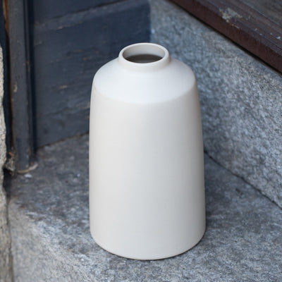 Simple matt beige flower vase stands on a stone staircase