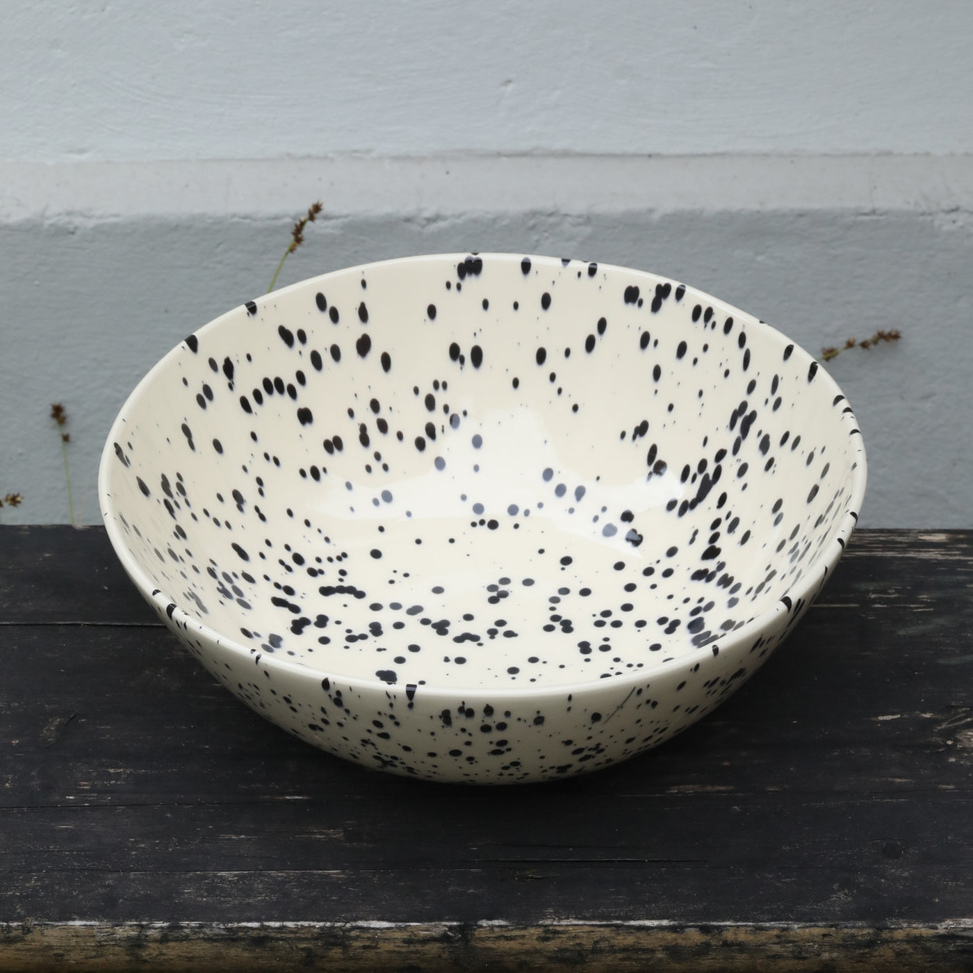 Beige salad bowl speckled with black spots of color on a woody background