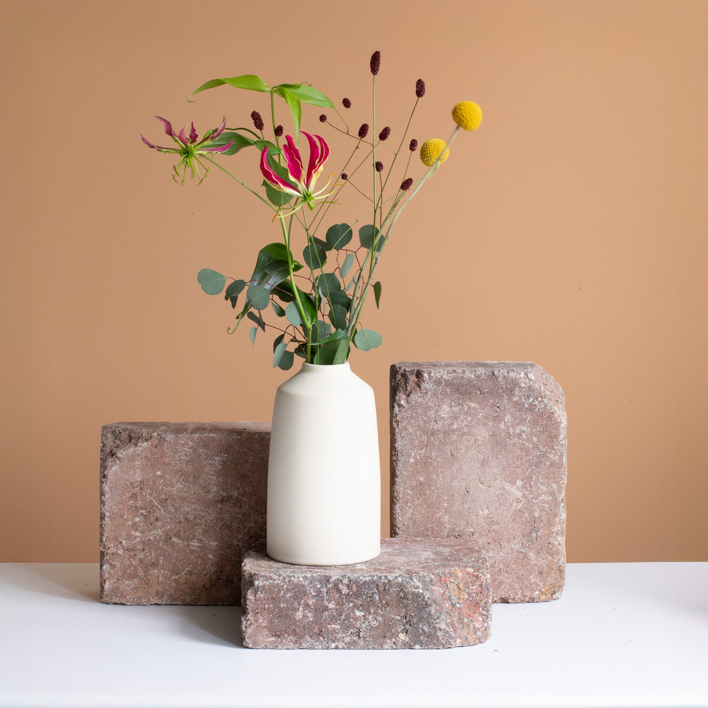 Cream-colored vase with a red and yellow flower rhinestone stands on a rust-brown brick