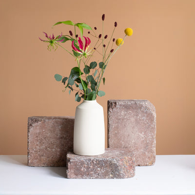Cream-colored vase with a red and yellow flower rhinestone stands on a rust-brown brick