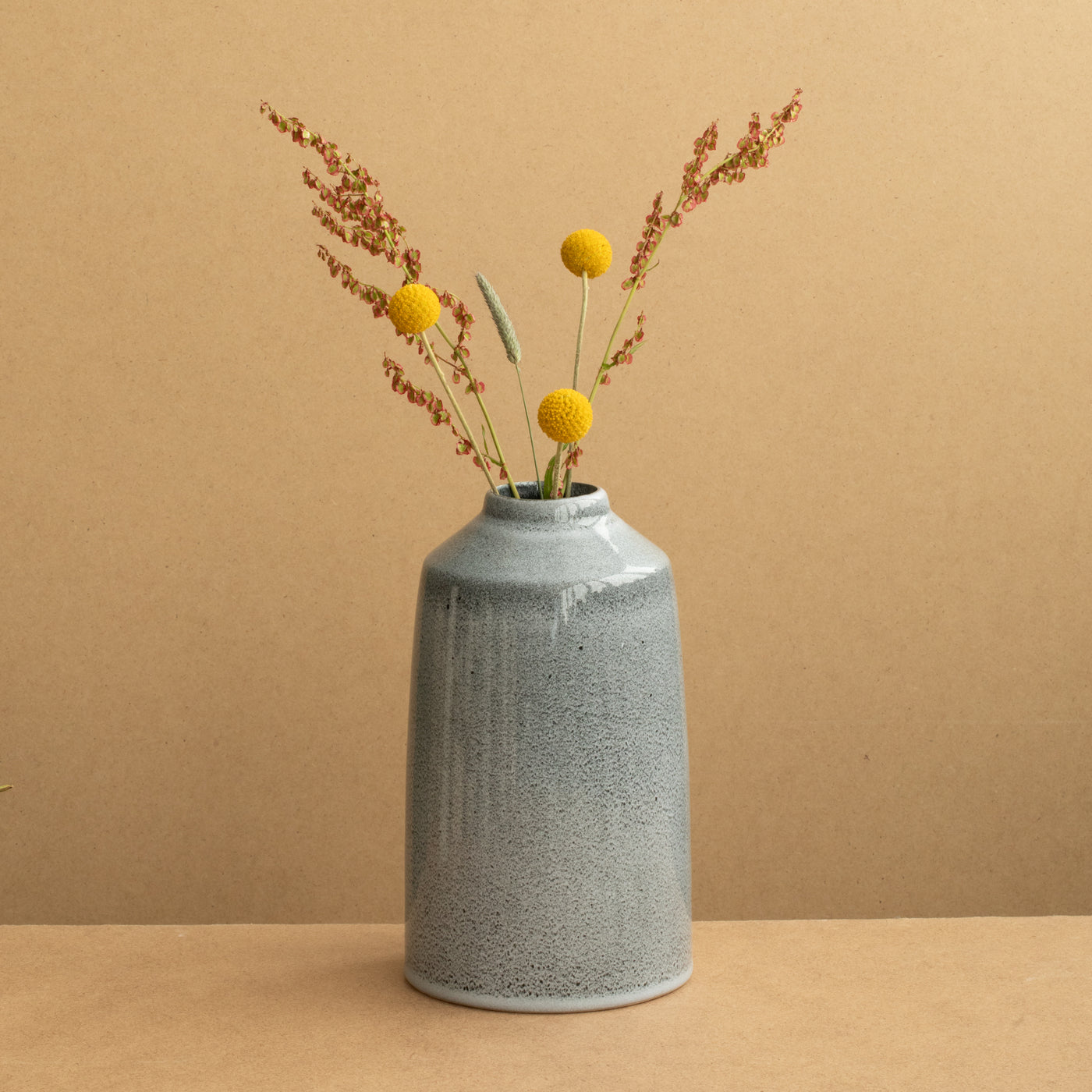 Blue flower vase with yellow flowers against a terracotta-colored background
