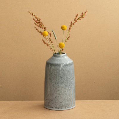 Blue flower vase with yellow flowers against a terracotta-colored background