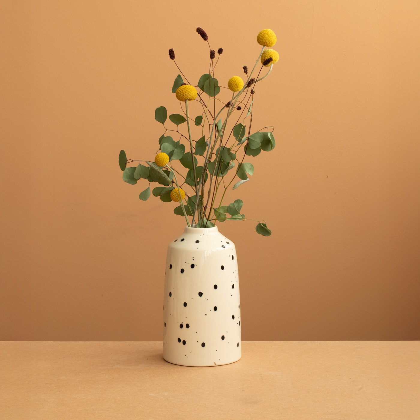 Bottle vase in beige color with black dots in it a green-yellow flower rhinestone in front of a warm terracotta background 
