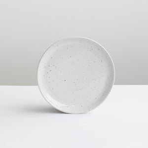 White small starter plate in white with fine golden speckles against a gray background