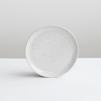 White small starter plate in white with fine golden speckles against a gray background
