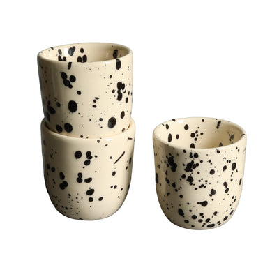 Two stacked and one adjacent beige espresso cup with black dots cut out against a white background.