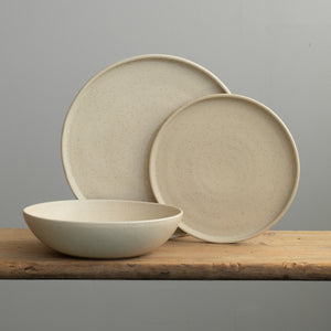 Tableware set in speckled beige with a large plate, a small plate and a deep pasta plate in front of it 