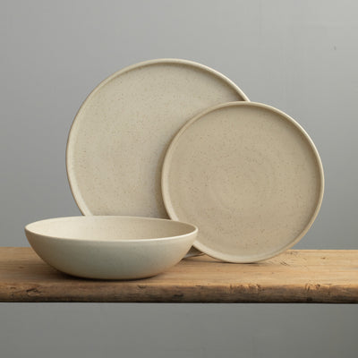 Tableware set in speckled beige with a large plate, a small plate and a deep pasta plate in front of it 