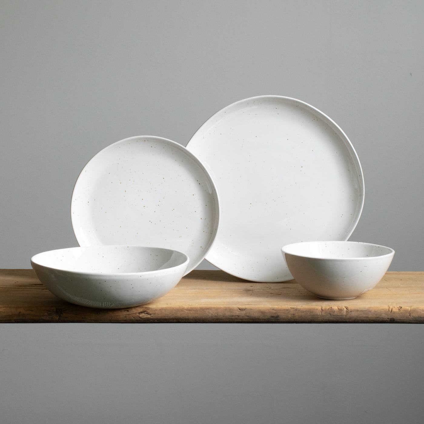 Four different types of plate on a wooden table. You can see a small and large plate placed on top of each other, in front of which is a pasta plate and a muesli bowl in white glaze with fine golden spots.