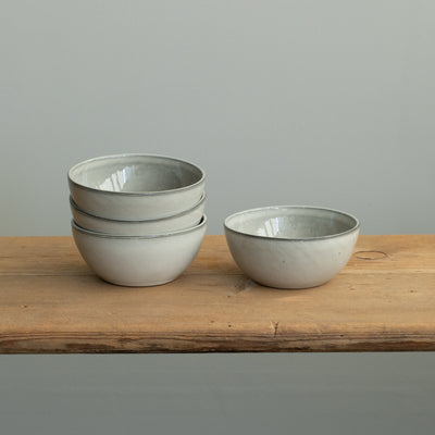 Three light gray bowls stacked on top of each other and a small bowl next to them on a wooden table