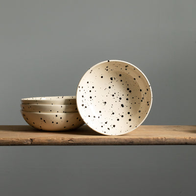 Beige main course plate with black splashes of color from the front and three stacked pasta plates