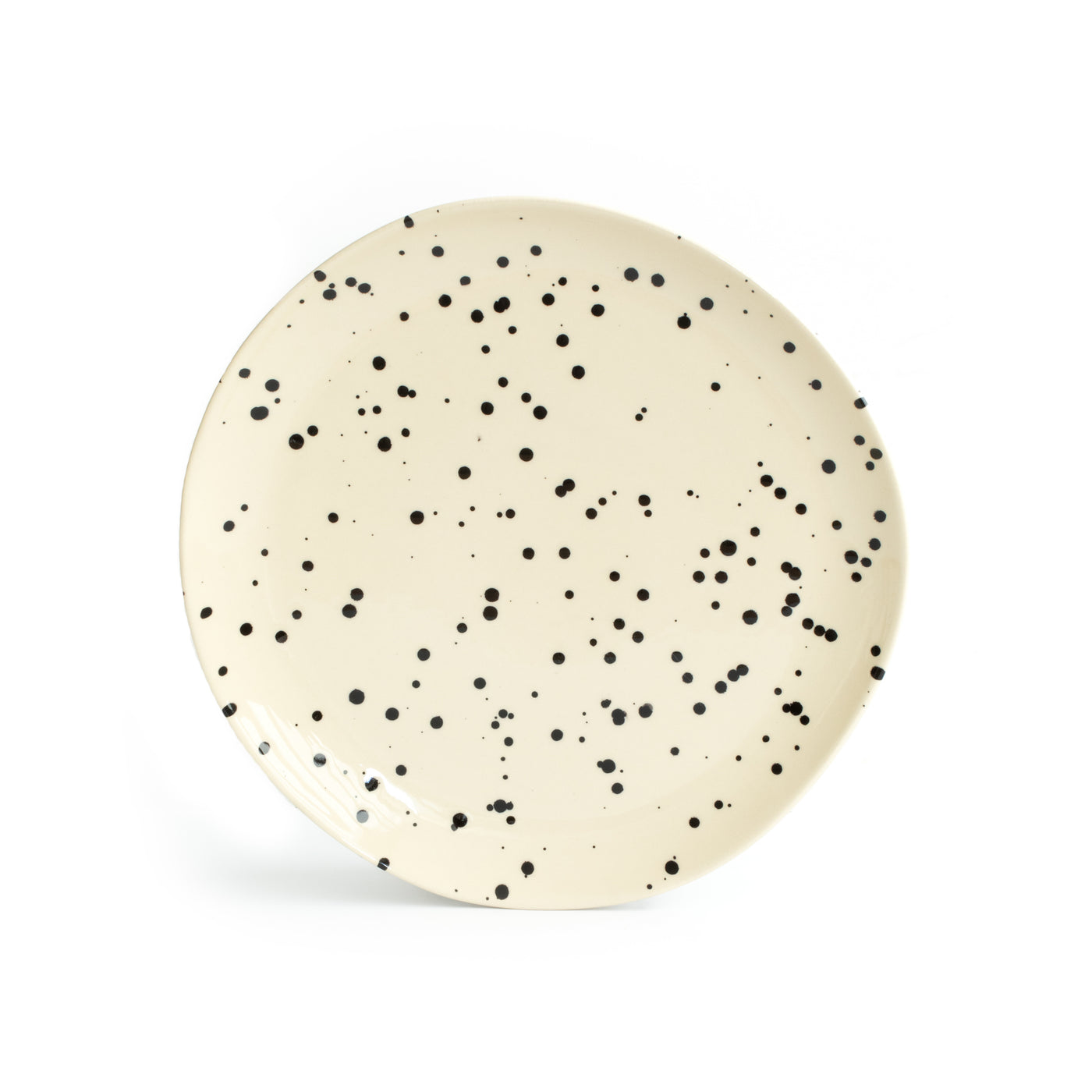 A large beige main course plate set up with splashes of black paint and cropped against a white background