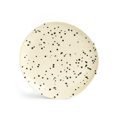 A large beige main course plate set up with splashes of black paint and cropped against a white background