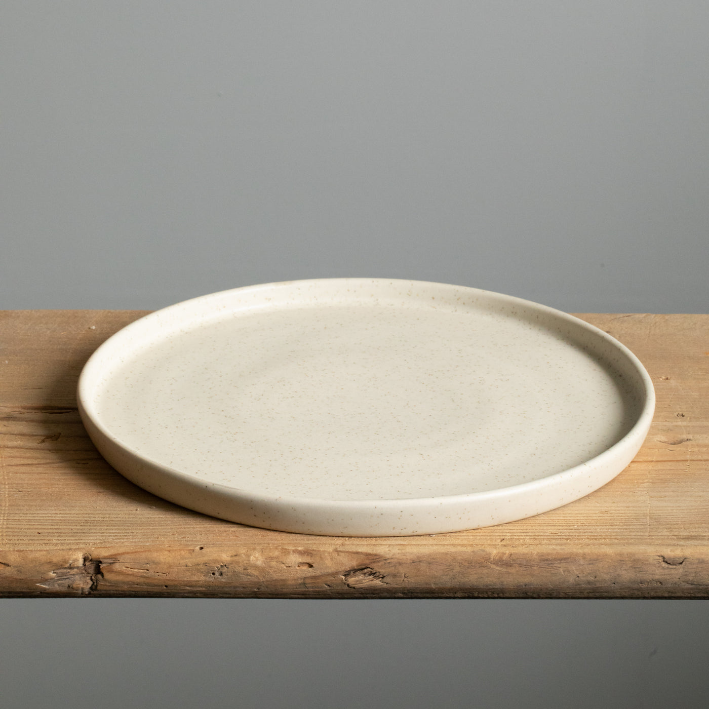 Matt beige large plate with straight rim lying on a wooden board