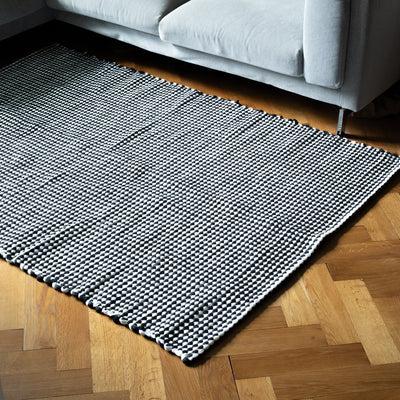 Large black and white carpet lies in front of a sofa on a wooden floor 