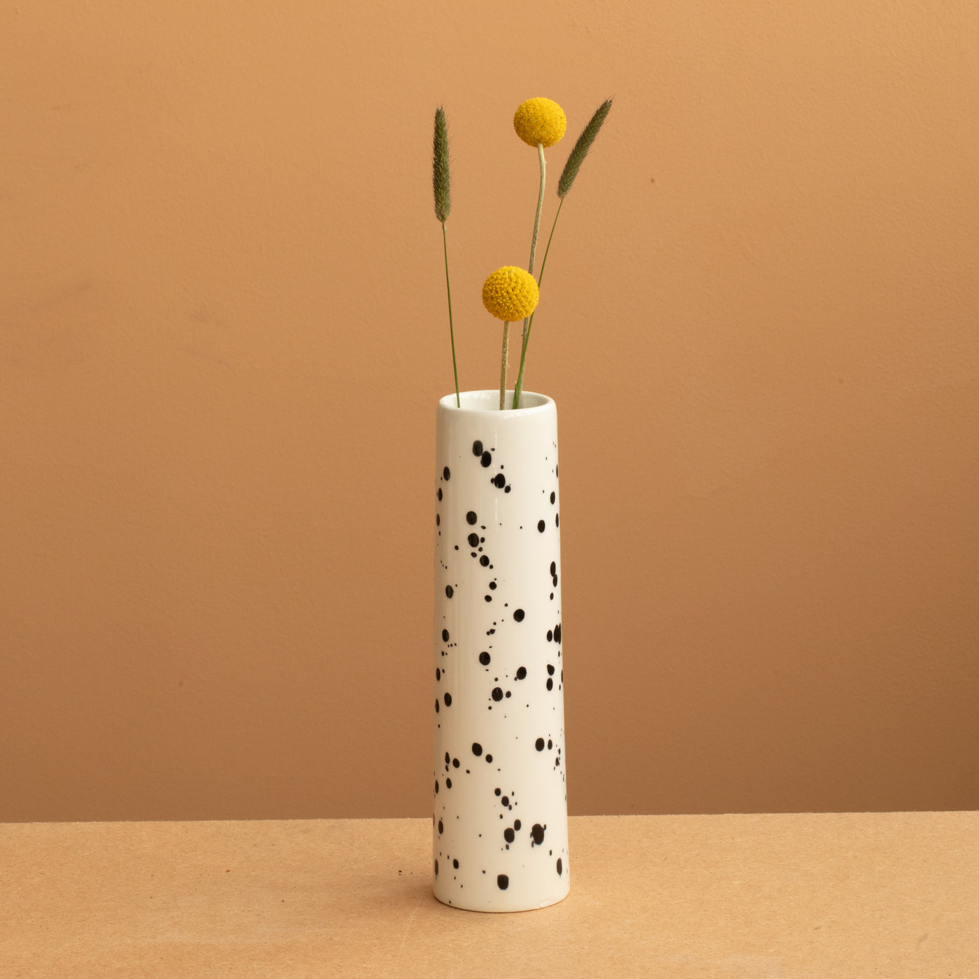 small narrow vase in beige color with black dots with yellow flowers.
