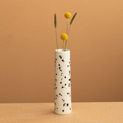 small narrow vase in beige color with black dots with yellow flowers.