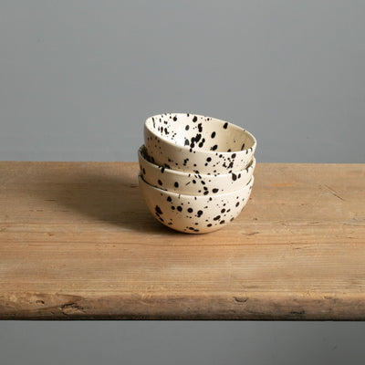 Three small snack bowls in cream with black splashes of color.stacked