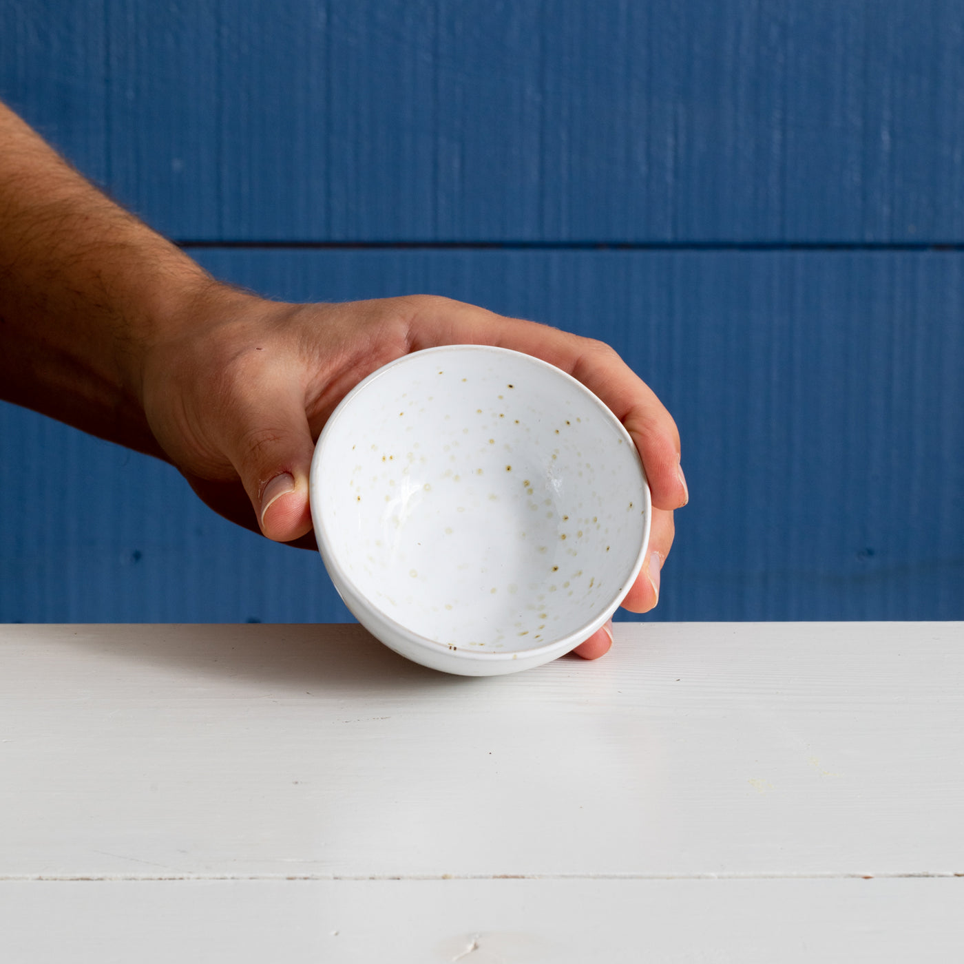 Small round ceramic snack bowl in white glaze with golden dots is held upright by a hand