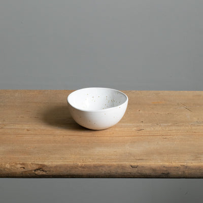Small white bowl with golden sprinklers from above on a wooden board