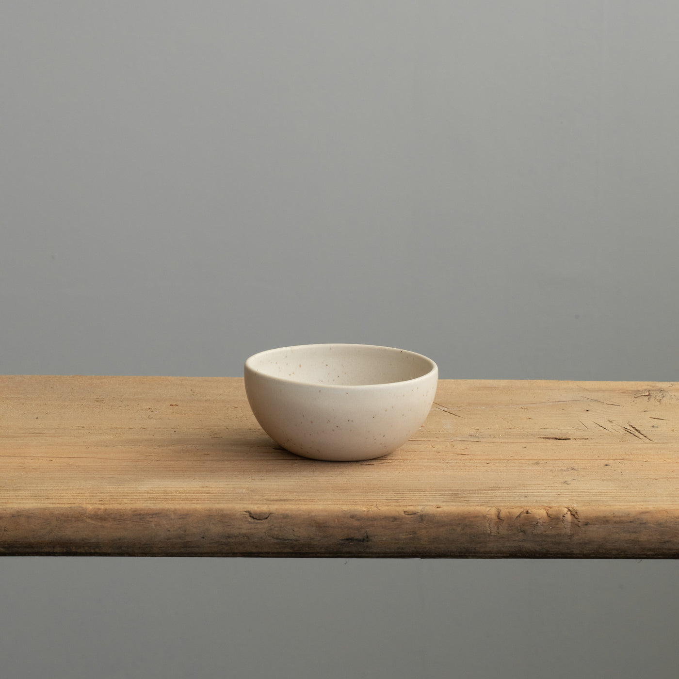 Front view of a small beige bowl in matt glaze on a wooden table
