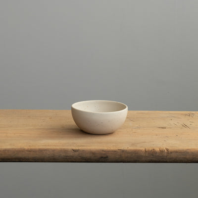 Front view of a small beige bowl in matt glaze on a wooden table