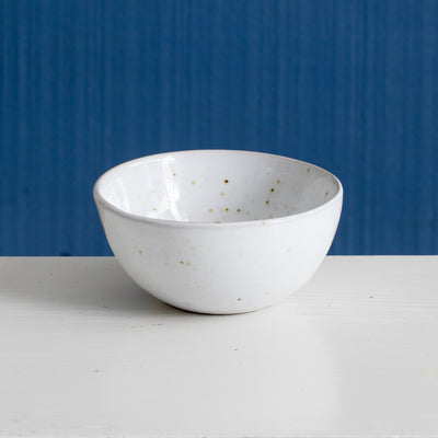 Small dip tray with white reactive glaze and golden speckles against a blue background