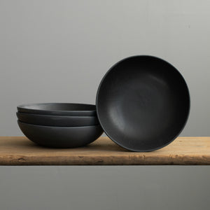 Matt black stoneware pasta plate stacked on a wooden table
