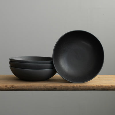 Matt black stoneware pasta plate stacked on a wooden table